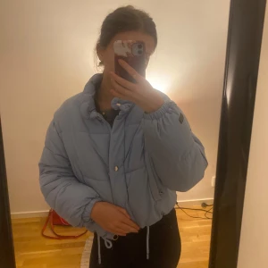 Ljusblå pufferjacka - Säljer en supermysig ljusblå pufferjacka i bra skick. Den har en dragkedja och knappar framtill, samt långa ärmar. Perfekt för höst och vinter när du vill hålla dig varm och snygg. Jackan har en loose passform och är riktigt bekväm. Något kort i formen (men väldigt varm och go) men det är meningen!