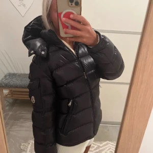 Svart dunjacka från Moncler - Säljer en snygg och varm svart dunjacka från Moncler some modell Maya. Jackan har en huva och dragkedja framtill, perfekt för kalla vinterdagar. Den är i mycket bra skick och har en stilren design med Moncler-loggan på ärmen. Passar perfekt för både vardag och fest!💕💋pris kan diskuteras eftersom inne lappen är halvt av är priset lågt