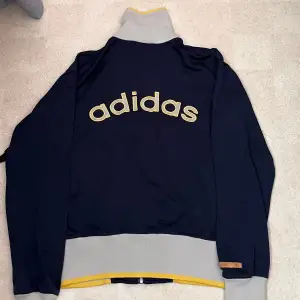 Säljer trackjacket från Adidas med dragkedja för 90talet.Den har en hög krage. Perfekt för höst och vår, och funkar lika bra till träning som till vardags. Stor logga på ryggen 