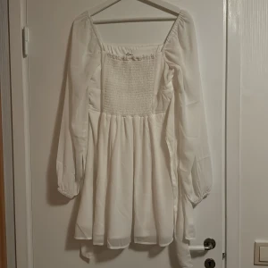 Vit klänning med smockdetalj - Säljer min utspringsklänning från studenten, jätte fin och lätt i materialet. Långa tunna armar med en rosett bak i ryggen, strl 36