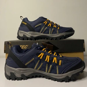 Blå och gula sneakers från Hi-Tec - Säljer ett par snygga och robusta sneakers från Hi-Tec i blått med gula detaljer. Skorna har en slitstark sula och är perfekta för utomhusaktiviteter. De är märkta som veganska och har en bekväm passform med snörning. Perfekta för både vardag och äventyr!