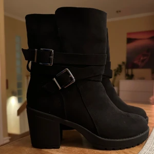 Svarta boots med spännen - Snygga svarta boots i mocka med robust klack och coola spännen. Perfekta för höst och vinter. De är helt nya, med lapp kvar under skon. 