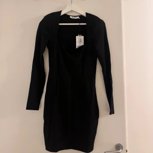 Svart klänning från NA-KD - Snygg svart kortklänning från NA-KD i nytt skick med lappen kvar. Den har en tight passform och är långärmad med axelvaddar. Går bra att dressa upp och ner.