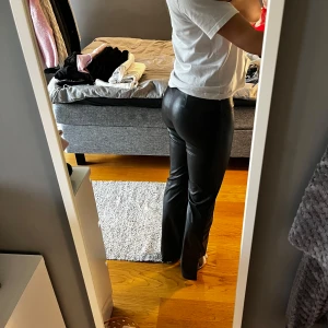 Svarta skinnbyxor - Snygga svarta skinnbyxor i syntetmaterial. De är högmidjade och har en tight passform som framhäver figuren. Byxorna har en slät yta och är i mycket bra skick. Minns ej var de är köpta. Slits på utsidan av benet. 