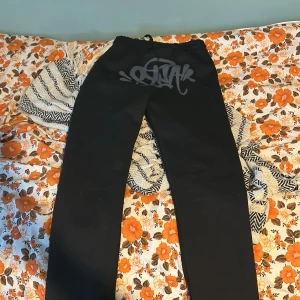 Svarta mjukisbyxor med tryck - Säljer ett par svarta mjukisbyxor i bra skick. De har ett coolt tryck med texten 'Forgive Me' på benet och en snörning i midjan för perfekt passform. Perfekta för en avslappnad dag hemma eller en chill dag ute. Passar bra till höst och vinter.
