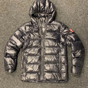 Canada Goose jacka - Säljer en snygg svart pufferjacka från Canada Goose. Jackan har en praktisk huva och dragkedja framtill. Perfekt för kyliga dagar och håller dig varm och stilren. Den är i mycket bra skick och passar perfekt för höst och vinter.              Storlek barn XL sitter som S 