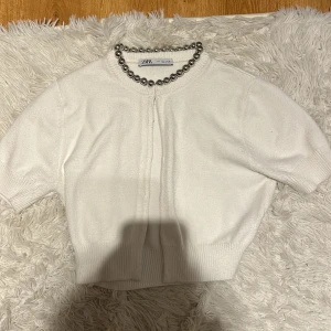 Vit kortärmad kofta från Zara - Säljer en superfin vit kofta från Zara med korta ärmar och en snygg pärldetalj. Ribbstickad nederkant ger en skön passform. Har aldieg kommit till användning 💕
