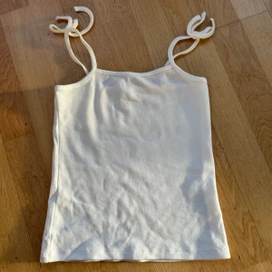 Vit ribbad linnetopp från Nelly  - Säljer en superfin vit ribbad linnetopp från Nelly Trend i storlek XS. Toppen har smala axelband som knyts, vilket ger en söt detalj. Perfekt som ett basplagg i garderoben. Aldrig använd så den är i mycket bra skick. 🤍