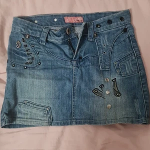 Jeanskjol från QS1 Jeans Wear - Säljer en cool jeanskjol från QS1 Jeans Wear. Den är blå med snygga detaljer som nitar och broderier. Kjolen har flera fickor och en unik design. Passar folk med strl S/XS
