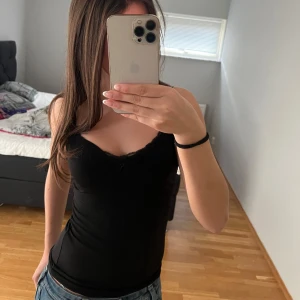 Svart ärmlös topp - Säljer en stilren svart ärmlös topp i mycket bra skick. Perfekt för sommardagar eller som basplagg under en jacka. Toppen har en tight passform och är gjord i ett mjukt och stretchigt material. 