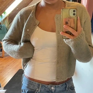 Beige/grön stickad kofta - Säljer en supermysig beige stickad kofta med knappar framtill. Perfekt för kyliga dagar och passar till allt! Koftan har långa ärmar och en skön passform. Perfekt för höst och vinter. 🧥✨