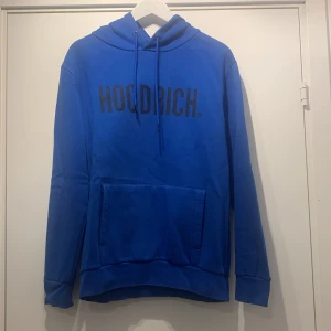 Blå hoodie från Hoodrich - Säljer en snygg blå hoodie från Hoodrich i bra skick. Den har en stor ficka fram och justerbar huva med dragsko. Perfekt för höst och vinter, och passar både till vardags och chill. Stor logga på bröstet ger en cool look. Hör av dig vid intresse! 💙