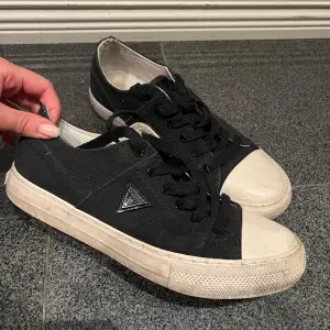 Säljer ett par svarta Guess sneakers med vit sula och snörning. De har en klassisk design med en liten logga på sidan. Perfekta för vardagsbruk och passar till det mesta. Lite slitna men fortfarande i bra skick.