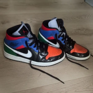 Färgglada Nike Air Jordans - Säljer ett par coola och färgglada Nike Air Jordans i storlek 40. Skorna har en mix av svart, orange, blå, grön och röd färg med klassisk snörning. Perfekta för att sticka ut och ge din outfit en unik touch. Använda men i bra skick!