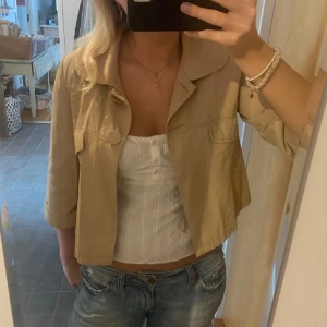 Beige croppad jacka - Säljer en superfin beige croppad jacka med trekvartsärm. Perfekt för vår och sommar! Den har stora knappar framtill och en stilren design som passar till allt. 