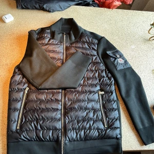 Svart Moncler Cardigan - Säljer en snygg svart Moncler jacka i mycket bra skick. Storlek S! Har en defekt på armen som du ser på en av bilderna, annars er den som ny.Perfekt för sen höst och vinter.Inte 100 vis jackan är ekta köpte av en kompis! Det är bara att skriva privat om flera bilder eller andra frågor om jackan😁
