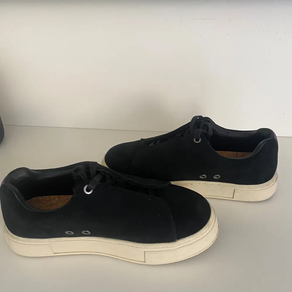 Säljer ett par stilrena svarta sneakers i mocka med vit sula. De har snörning och en klassisk design som passar perfekt till vardags. Skorna är i bra skick och har en bekväm passform. Perfekta för både vår och höst! Använda endast en gång så nästen helt nyskick. . Skor.