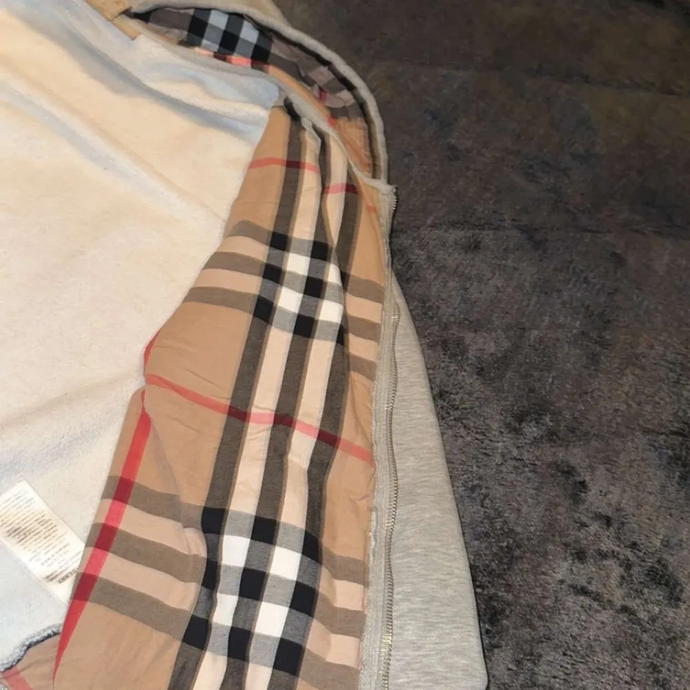 Säljer en snygg grå huvtröja från Burberry i storlek M. Den har en klassisk rutig insida i huvan och dragkedja framtill. Perfekt för höst och vår, med en stilren look som funkar till det mesta. Passar både till vardags och lite finare tillfällen.. Hoodies.