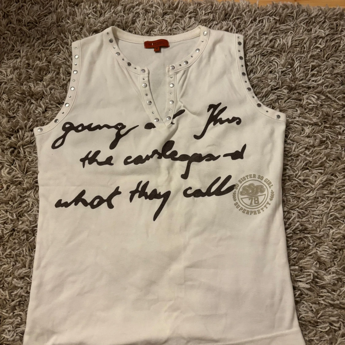 Vit ärmlös topp med text och nitar