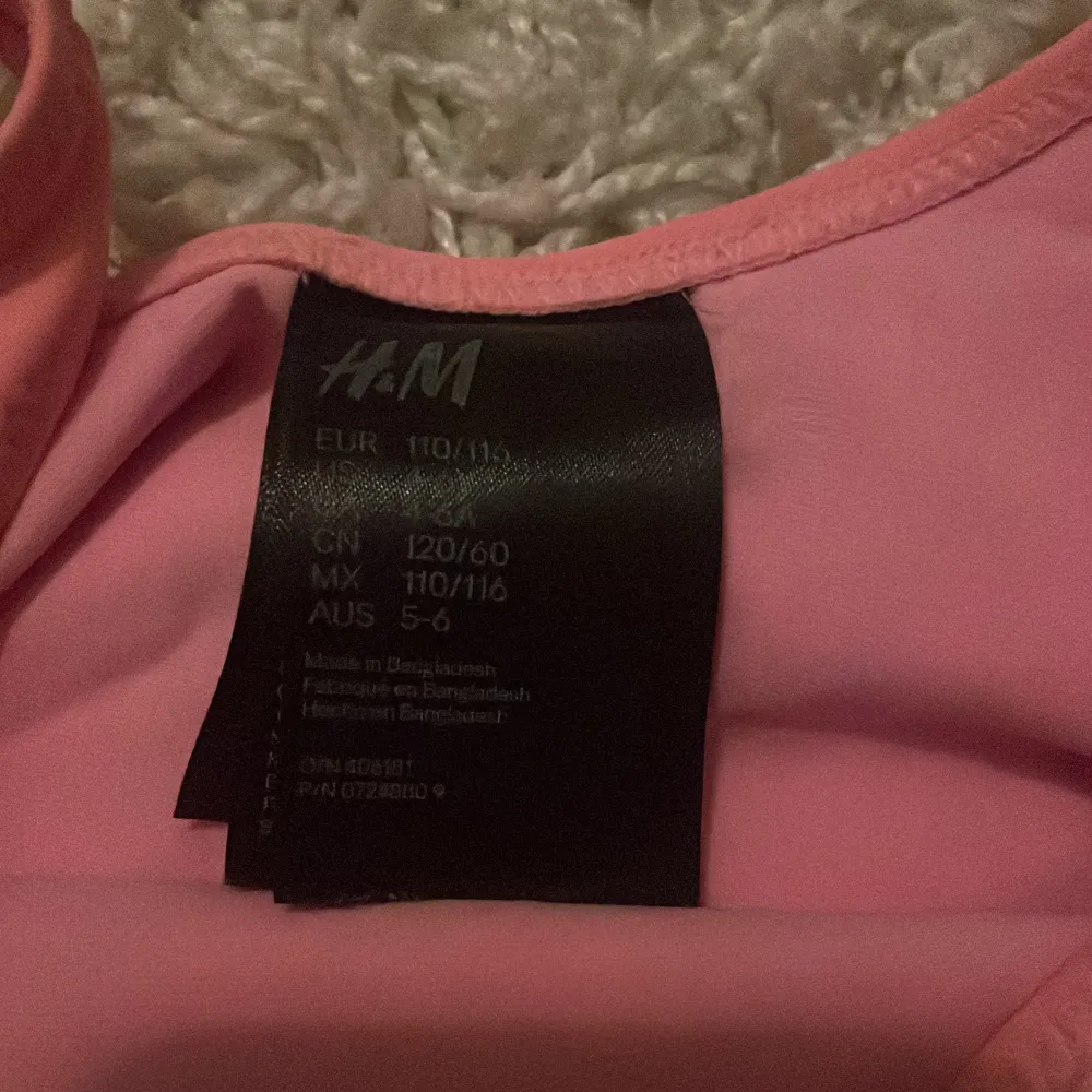 Superfin rosa baddräkt från H&M med ett coolt ananastryck och texten 'Summer!' på framsidan. Perfekt för sommarens badäventyr! Den har breda axelband och är gjord i ett mjukt och bekvämt material. Passar barn i storlek 110/116. 🌞🍍. Övrigt.