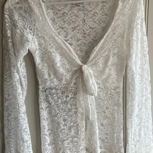 Vit spetsblus med knyt - Säljer en superfin vit spetsblus med knyt framtill. Den har långa ärmar och ett vackert blommigt mönster i spetsen