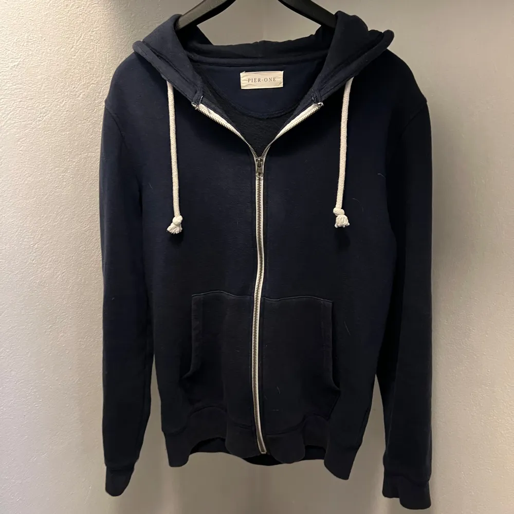 Säljer en snygg mörkblå hoodie från Pier One. Den har en dragkedja framtill och vita snören i huvan. Perfekt för en avslappnad stil och passar bra till både höst och vår. Den är i toppenskick.. Tröjor & Koftor.