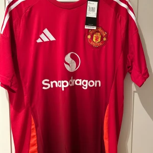 Röd Manchester United fotbollströja - Säljer en röd Manchester United fotbollströja från Adidas i nytt skick. Tröjan har korta ärmar och vita detaljer, inklusive klubbens emblem på bröstet. Perfekt för fans som vill visa sitt stöd på matchdagar! 🏟️ Den är även helt ny aldrig använt och pris kan diskuteras 
