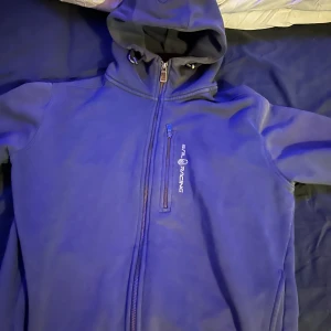 Blå hoodie från Sail Racing - Säljer en snygg blå hoodie från Sail Racing i bra skick. Den har en dragkedja framtill och en praktisk huva. Perfekt för höst och vår, och den är superbekväm att ha på sig. Passar både till vardags och lite mer avslappnade tillfällen.
