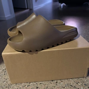 Yeezy slides bruna - Tja, säljer ett par bruna Yeezy slides från adidas och är i storleken 43 de är lite små i storleken så skulle säga att de passar de som har storleken 42 bättre än de som har storleken 43. De är ganska slitna o använda men mest bara under tofflorna. Skick 4/10 (box ingår)