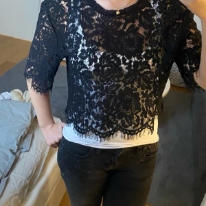 Svart spetsblus från Amisu - Säljer en elegant svart spetsblus från Amisu i storlek S. Blusen har ett vackert blommönster och trekvartsärmar. Perfekt för en festlig kväll eller en stilfull dag på stan. Den är croppad och ger en chic look över en enkel topp. Exklusive frakt.