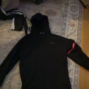 Svart hoodie. Äkta alpha.  - Fräsch hoodie med blixtlås på armen, med Alphaloggan. Två sidfickor. Använd typ tre gg.