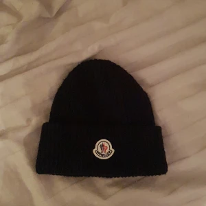 Moncler mössa - Säljer denna moncler mössa i nytt skick eftersom den är använd Max 2 gånger!🙌 säljer denna på grund av att jag inte använder den! Skulle kunna gå ner i pris vid snabb affär💸🤝 och hör av dig vid frågor!😊
