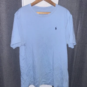 Ljusblå t-shirt från Ralph Lauren - Säljer en snygg ljusblå t-shirt från Ralph Lauren i bra skick. Den har en klassisk passform och är kortärmad med det ikoniska broderade logotypen på bröstet. Perfekt för både vardag och avslappnade tillfällen. Skön och stilren, ett måste i garderoben! 💙