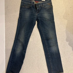 Lågmidjade blå jeans från Replay - Säljer ett par snygga blå jeans från Replay i modellen pearl. De är lågmidjade och uppvikta nedtill. De har coola detaljer både fram och bak! Lappen med storlek är bortklippt men skulle säga att de sitter som 34-36 i vanliga eu dam storlekar