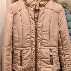 Säljer en snygg beige / skär pufferjacka från H&M i storlek XS. Jackan har en mysig fuskpäls på huvan ( är avtagbar)och stängs med dragkedja och knappar i halsen. Perfekt för kyliga höst- och vinterdagar. Den har långa ärmar och praktiska fickor med dragkedja. Superfin och i bra skick!