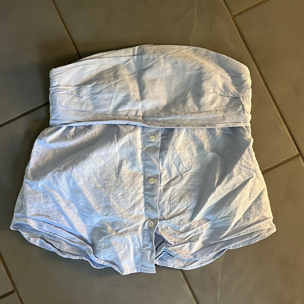 Säljer en söt ljusblå axelbandslös topp med knappar framtill. Perfekt för sommardagar eller en avslappnad fest. . Yläosat.