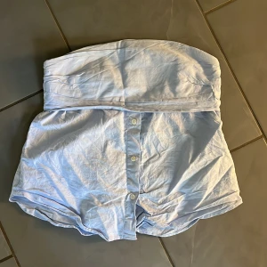zara topp - Säljer en söt ljusblå axelbandslös topp med knappar framtill. Perfekt för sommardagar eller en avslappnad fest. 
