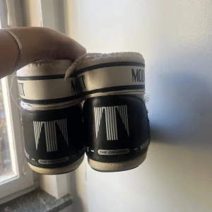 Svartvita Moon Boots - Säljer ett par klassiska Moon Boots i svart och vitt. De är perfekta för vintern med sin varma och vadderade design. Skorna har snörning och en robust sula för bra grepp. De är i bra skick med några mindre tecken på användning. Perfekta för kalla dagar! ❄️ Storlek 36/38
