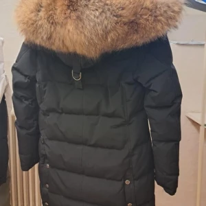 Svart dunjacka med pälsdetalj från Hollies - Säljer en snygg svart dunjacka från Hollies med stor, fluffig pälsdetalj på huvan. Jackan är i bra skick, använd en vinter. Storlek 34