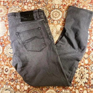 Jacob Cohen Jeans grå - Säljer ett par snygga grå jeans från Jacob Cohen. De har en klassisk femficksdesign och en bekväm passform. Jeansen är i mycket bra skick och har en stilren look med dragkedja och knapp. Perfekta för både vardag och fest!