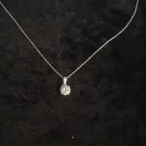 Elegant silverhalsband med en glittrande rund sten som hänge. Perfekt för att lägga till lite extra bling till din outfit, oavsett om det är till vardags eller fest. Kedjan är tunn och smidig, vilket gör den bekväm att bära hela dagen.