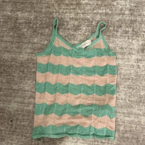 Randig linne från KIDS ONLY - Säljer ett supergulligt linne från KIDS ONLY i storlek 134/140. Det har ett randigt mönster i mintgrönt och rosa med smala axelband. Den är glittrig men inte obekväm. Perfekt för sommardagar eller som ett lager under en kofta. Linnet är i bra skick och redo för en ny ägare! 