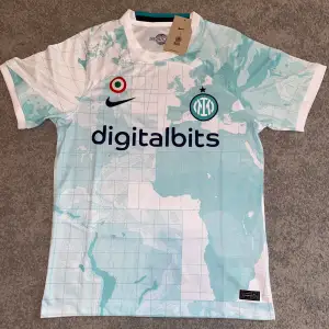 Säljer en snygg Inter Milan fotbollströja från Nike i ljusblått och vitt med ett unikt kartmönster. Tröjan är kortärmad och har digitalbits som sponsorlogga på framsidan. Perfekt för alla Inter-fans! 🖤💙