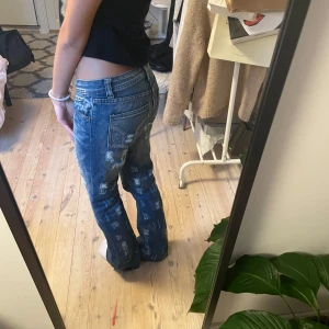 Blå jeans med slitningar - Säljer ett par snygga blå jeans med en cool slitningar som tillhör designen av jeansen. De är lågmidjade o har en normal passform. Dom är lite långa på mig som är 160cm💝. Märket okänt då dom köpta vintage