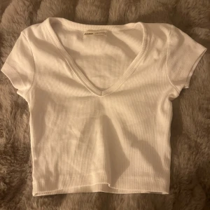 Vit v-ringad topp från Pull&Bear - Säljer en superfin vit v-ringad topp från Pull&Bear i storlek S. Den har en snygg v-ringning och korta ärmar, perfekt för sommardagar eller som ett basplagg i garderoben. Toppen är i mycket bra skick 