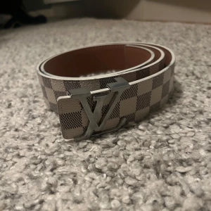 Bälte  - Snyggt bälte med ett klassiskt rutigt mönster och ett stilrent silverfärgat spänne. Perfekt för att ge en touch av elegans till din outfit. 110 cm, skriv för minsta frågor eller funderingar 