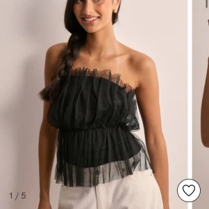 Svart axelbandslös topp med volang - Snygg svart axelbandslös topp med volangdetaljer och elastisk midja. Perfekt för en stilren look.