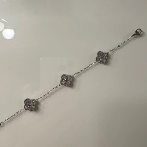 Silverarmband med klöver  - Silverarmband med tre klövrar, varje klöver har en glittrig design på ena sidan och en vit yta på den andra.