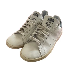 Vita Adidas Stan Smith sneakers - Klassiska vita Adidas Stan Smith sneakers perfekt till våren med snörning och perforerade detaljer på sidorna. Skorna har en ikonisk design med en bild på tungan och en bekväm sula. Perfekta för en stilren och tidlös look. OBS box följer ej med, varan kan vara sliten vid skosnörena men det går självklart att byta om man känner det