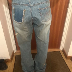 Blå jeans från Vila - Säljer ett par blå jeans från Vila med slitna detaljer och broderade bakfickor. Jeansen har en klassisk femficksdesign och dragkedjegylf. Perfekta för en avslappnad stil. De är använda men i bra skick!